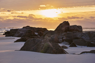 Rocks by sea against sky during sunset