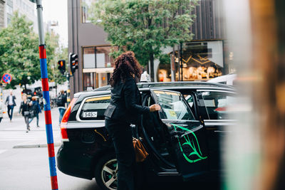 Mid adult businesswoman entering taxi on street in city