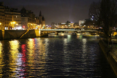 Illuminated buildings by river against sky at night