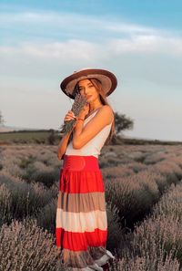 Portrait of woman holding flowers while standing on field against sky