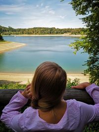 Rear view of woman sitting by lake against trees