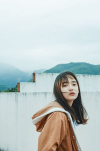 Side view portrait of young woman standing against sky