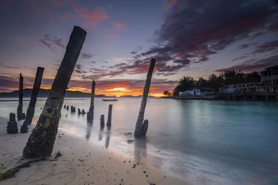 Wooden posts on beach against sky during sunset