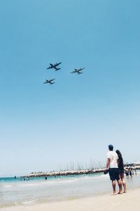 People enjoying at beach against clear blue sky