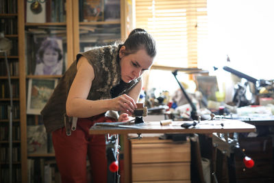 Girl master processes the metal copper plate on the workbench in the home workshop, soft focus 