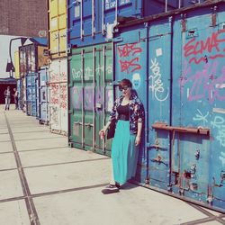 Fashionable beautiful woman standing with drink can against graffiti on cargo containers