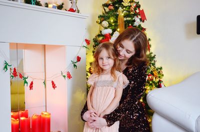 Mother with cute daughter standing by christmas tree at home