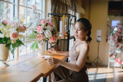 Side view of young woman sitting on table at home