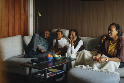 Family watching tv together while sitting on sofa at home