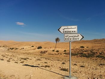 Road sign on desert against blue sky