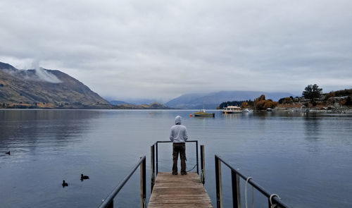 Rear view of man standing on pier over lake against sky