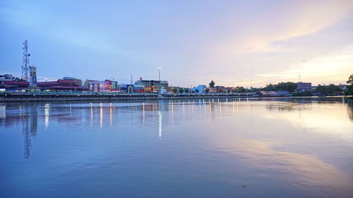 Scenic view of lake by buildings against sky during sunset