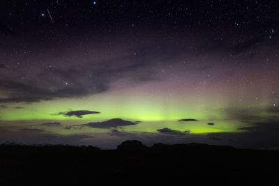 Picturesque scenery of amazing polar lights shining in dark starry sky over massive rocky mountains