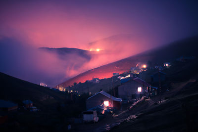 Illuminated houses by mountains at night during foggy weather