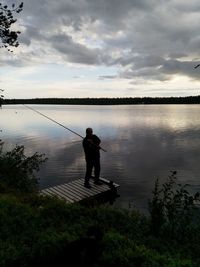 Man fishing in lake against sky