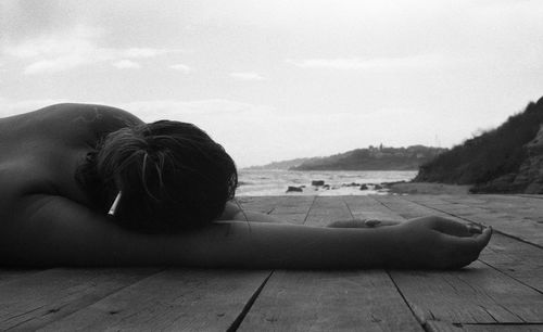 Rear view of woman relaxing on wood against sky