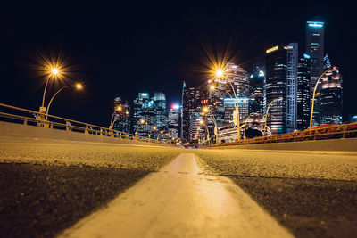 Illuminated street amidst buildings against sky at night