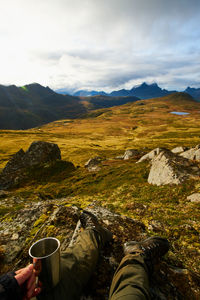 Hiker holding coffee cup with hand with mountains and landscape in the background on lofoten islands