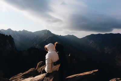 Rear view of people sitting on rock against mountains