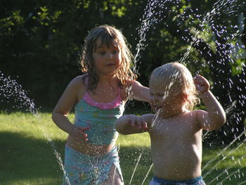Siblings standing by spraying water in park