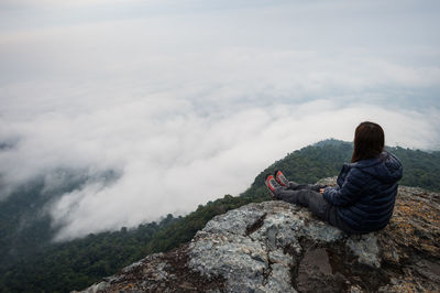 High angle view of woman sitting on rock formation at mountain peak during foggy weather