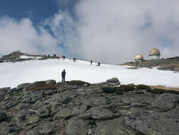 Rear view of man standing on rock against sky during winter