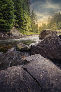 Stream flowing through rocks by river against sky