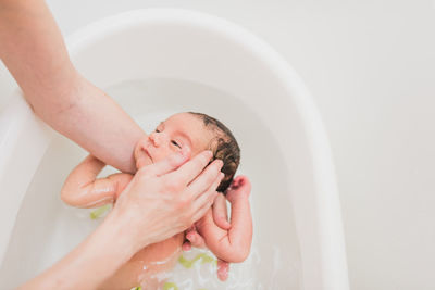 From above unrecognizable parent washing and touching face of crying newborn baby in warm water in basin at home