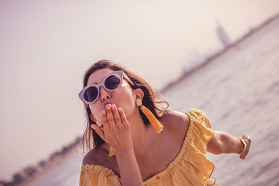 Woman blowing kiss while standing at beach