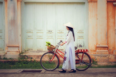 Woman with bicycle walking against wall
