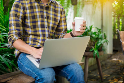 Midsection of man using mobile phone while sitting outdoors