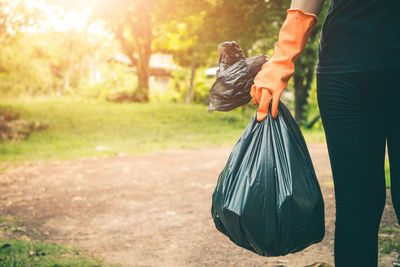 Midsection of woman holding garbage bag while standing on field