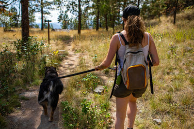 Rear view of woman with dog walking on dirt road