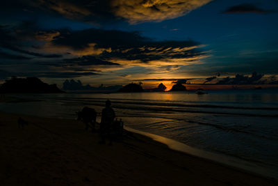 Silhouette people on beach against sky during sunset