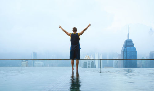 Man standing in infinity pool against sky in city