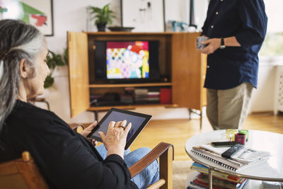 Senior woman using digital tablet while man standing at home