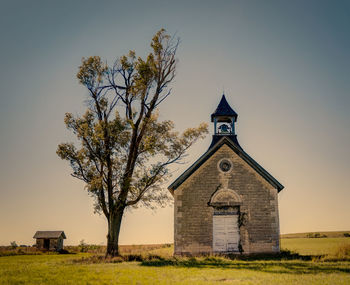 Low angle view of church and trees on grassy field against sky during sunny day