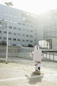 Female astronaut in space suit walking on footpath near building