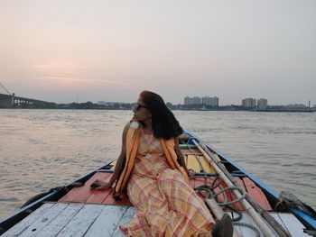 Woman sitting on boat in sea against sky during sunset