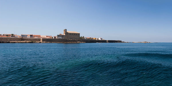 Sea by buildings against clear blue sky