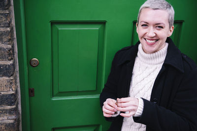 Cheerful woman with keys standing outside new home