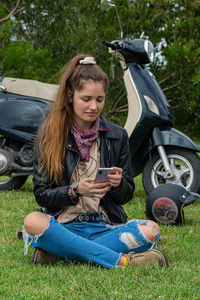 Young woman using a smartphone while standing by her motorbike