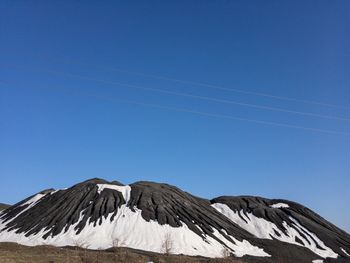 Low angle view of snowcapped mountains against clear blue sky