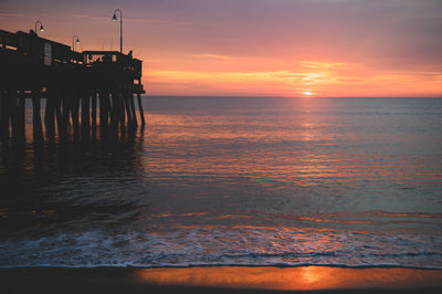 Scenic view of sea and fishing pier against orange and purple sky during sunrise