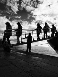 Silhouette people walking on ladder at ship against sky