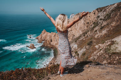 Woman standing on cliff against sea