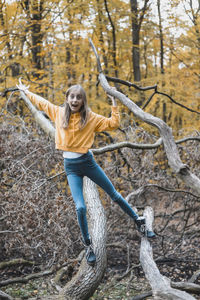 Portrait of scared girl with arms outstretched standing on tree trunk in forest