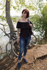 Brunette with a backpack and 2 bicycles on a sunny day against the background of the river.