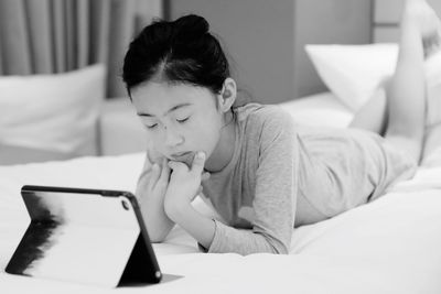 Girl using digital tablet while lying down on bed at home