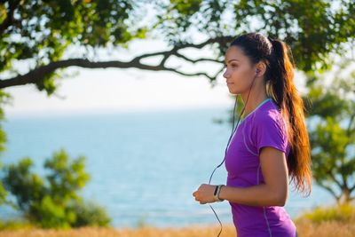 Side view of young woman standing by tree against sea